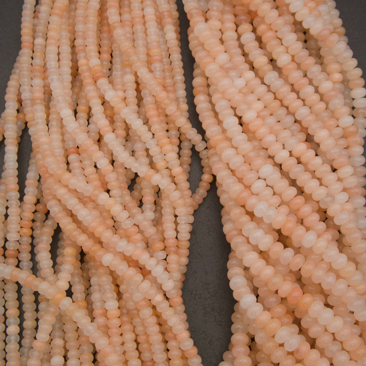 Multiple strands of small faceted round beads in a soft peachy pink color, arranged on a dark gray background.