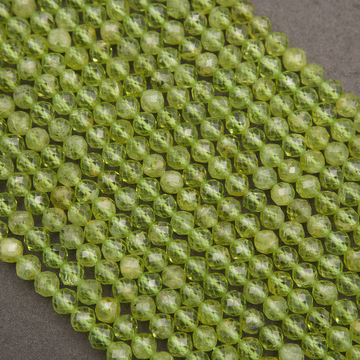 Faceted round beads in a translucent light olive green color, arranged in a diagonal pile on a dark gray background.