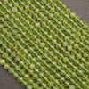 Faceted round beads in a translucent light olive green color, arranged in a diagonal pile on a dark gray background.
