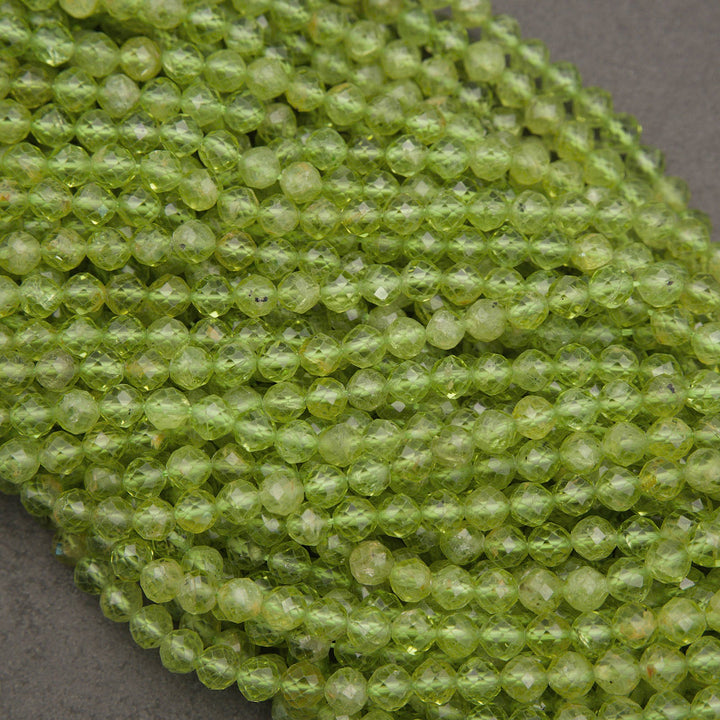 A close-up of many small faceted round beads in a translucent light yellow-green color, arranged in overlapping strands on a neutral gray surface.