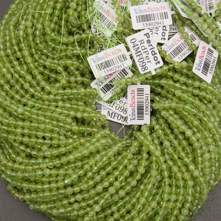 A large coil of light green faceted round beads with multiple white product tags attached, photographed close-up on a dark gray surface.