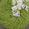 A large coil of light green faceted round beads with multiple white product tags attached, photographed close-up on a dark gray surface.