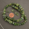 Green bead necklace with a penny for scale on a gray background