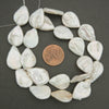 String of white teardrop-shaped pearls with a penny for scale on a dark background