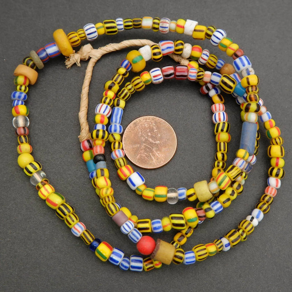 Colorful beaded necklace with a penny for scale on a dark surface