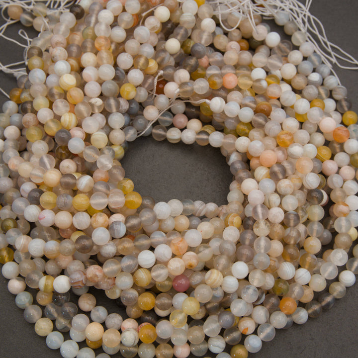 Coiled strands of round agate beads in natural stone colors, including gray, beige, white, and soft orange, on a dark gray background.