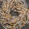 Coiled strands of round agate beads in natural stone colors, including gray, beige, white, and soft orange, on a dark gray background.