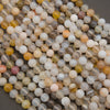 A close-up pile of round, polished agate beads in various natural stone colors including gray, white, yellow, brown, and pinkish tones, resting on a dark gray surface.
