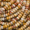 A close-up pile of polished oval beads in marbled cream, yellow, tan, and reddish-brown tones.
