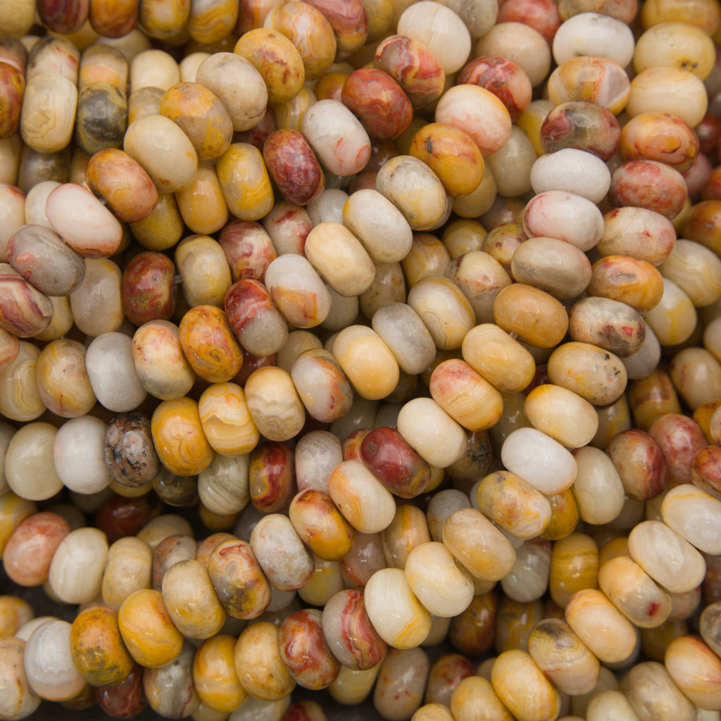 A close-up pile of polished oval beads in marbled cream, yellow, tan, and reddish-brown tones.