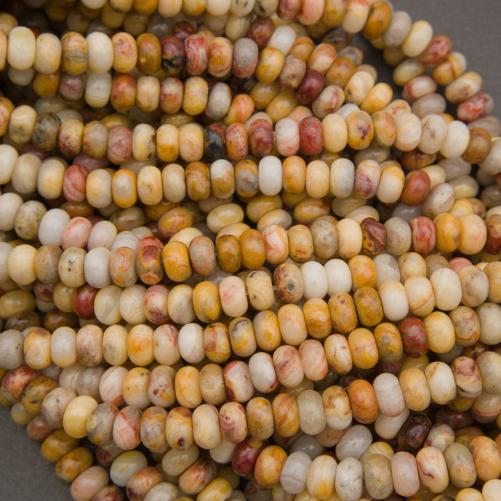 Close-up of a pile of small cylindrical beads with a marbled pattern in cream, yellow, orange, and reddish-brown tones.