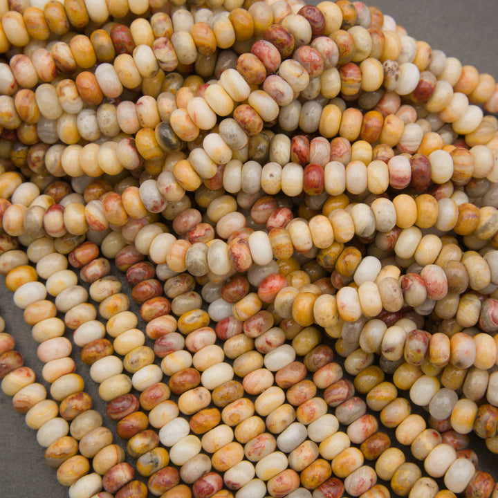 Close-up of multiple strands of small cylindrical beads with a marbled pattern in cream, yellow, orange, and reddish-brown tones on a neutral gray surface.