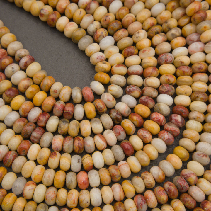 Curved strands of polished oval beads in a marbled mix of cream, yellow, orange, and reddish-brown tones on a dark gray background.