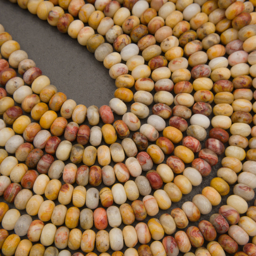 Curved strands of polished oval beads in a marbled mix of cream, yellow, orange, and reddish-brown tones on a dark gray background.