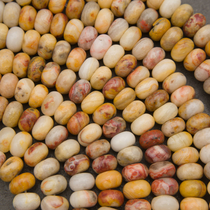 A close-up pile of polished oval beads in marbled cream, yellow, tan, and reddish-brown tones on a dark surface.