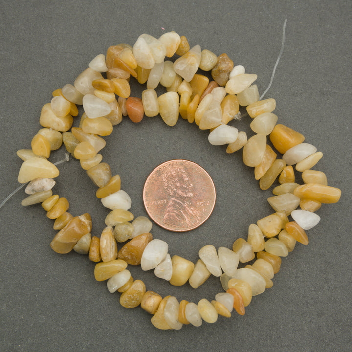 Necklace of small stones with a penny for scale on a gray background